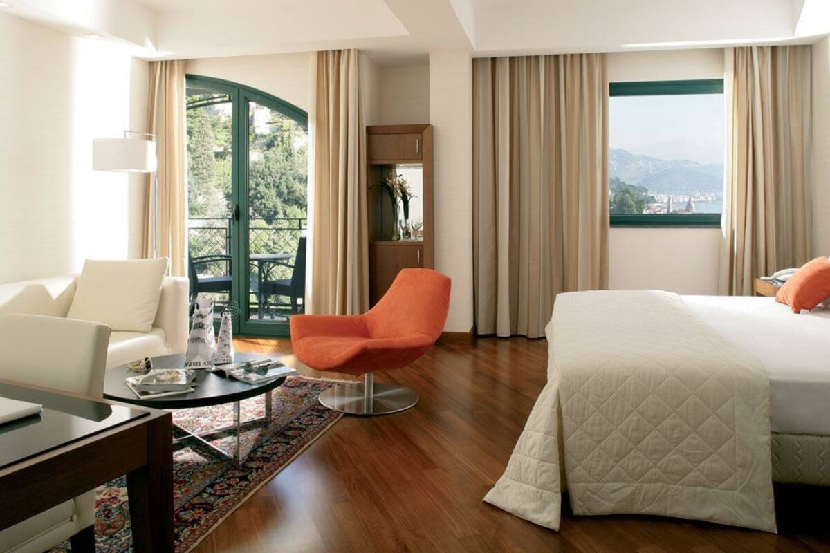 A hotel room with a bed, a desk, a chair, a balcony with a view, and a window.