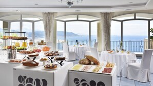 A breakfast buffet with a variety of pastries, fruits, and beverages, set in a room with large windows overlooking a scenic view.