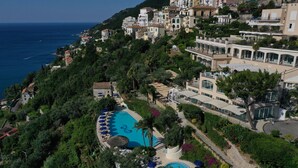A coastal resort with a swimming pool surrounded by lush greenery, overlooking the sea.