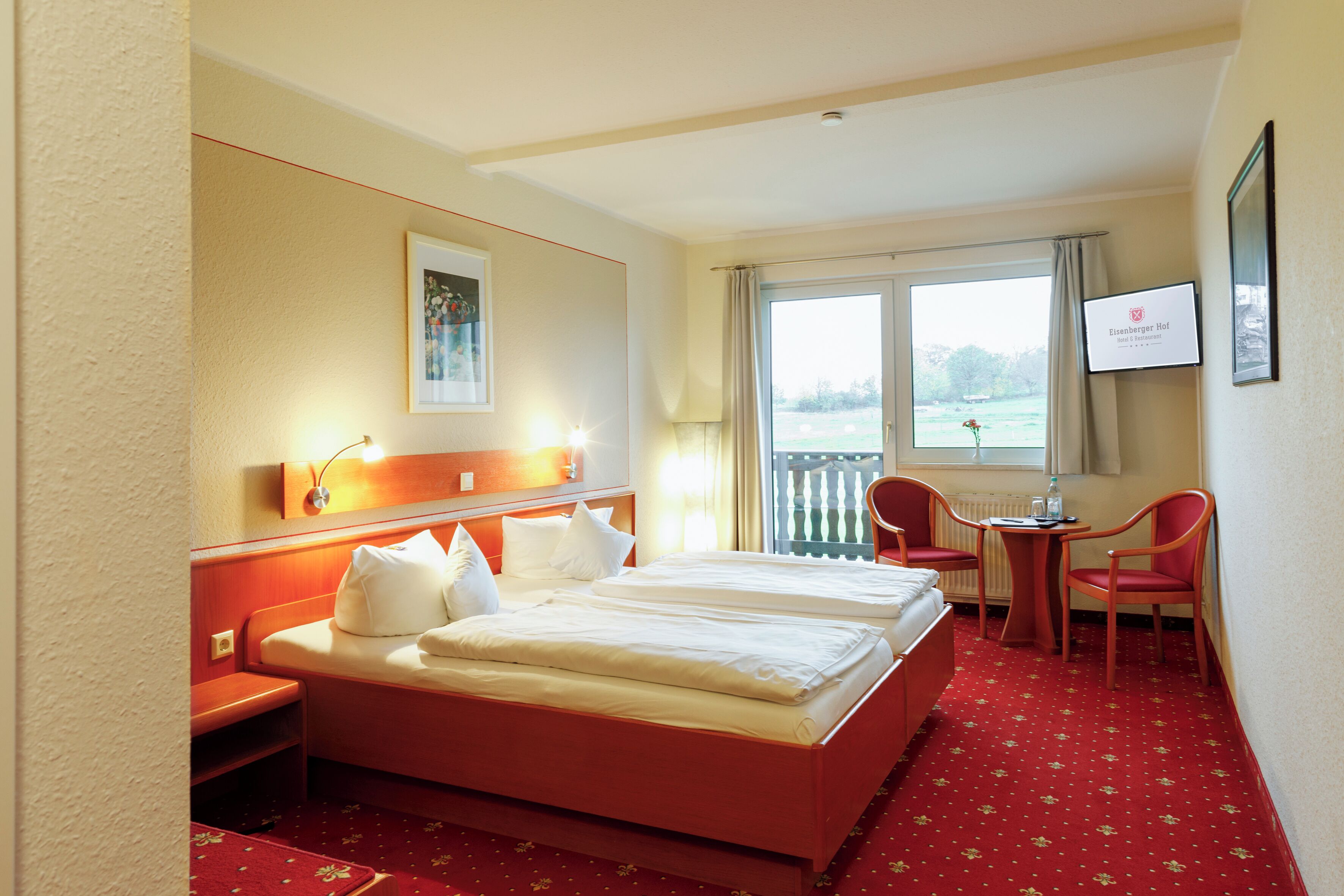 A hotel room with two beds, a desk, a chair, and a window with a view.