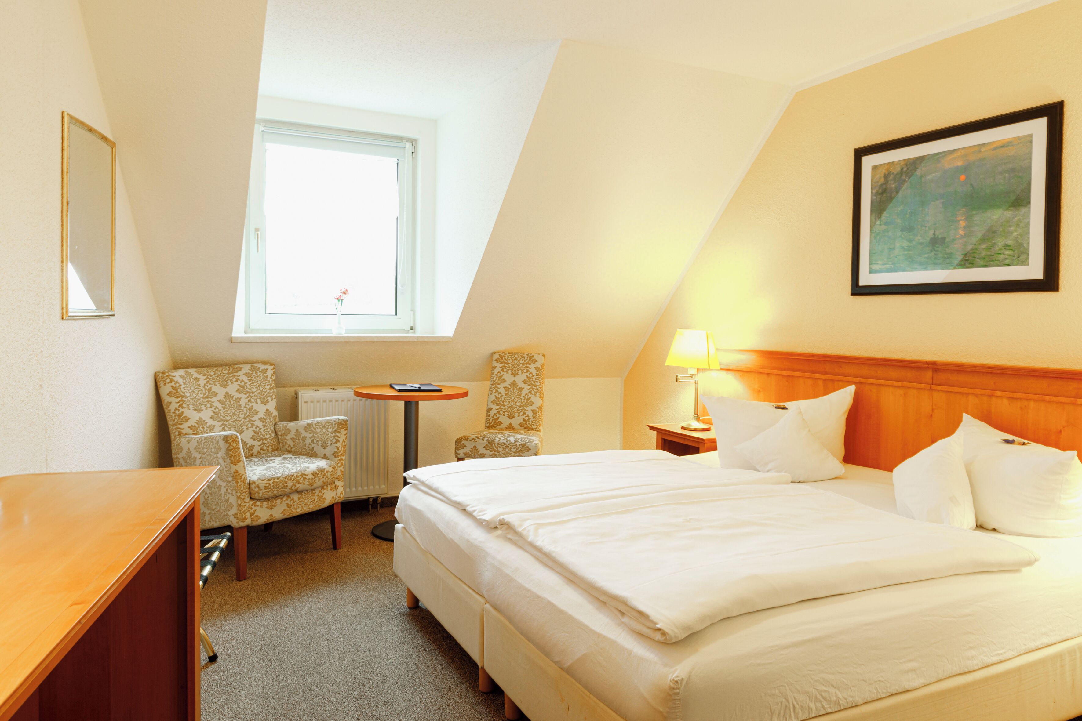 Ein Hotelzimmer mit einem großen Bett, einem Schreibtisch, einem Stuhl, einem kleinen Tisch und einem Fenster.