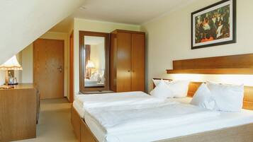 A hotel room with a large bed, a wooden wardrobe, a desk with a lamp, and a painting on the wall.