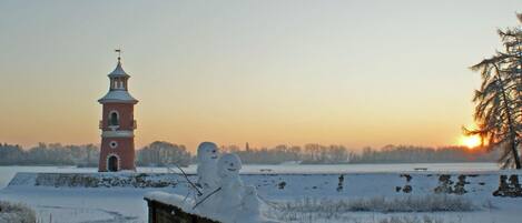 Paisagem coberta de neve com uma torre de tijolos vermelhos e dois bonecos de neve.