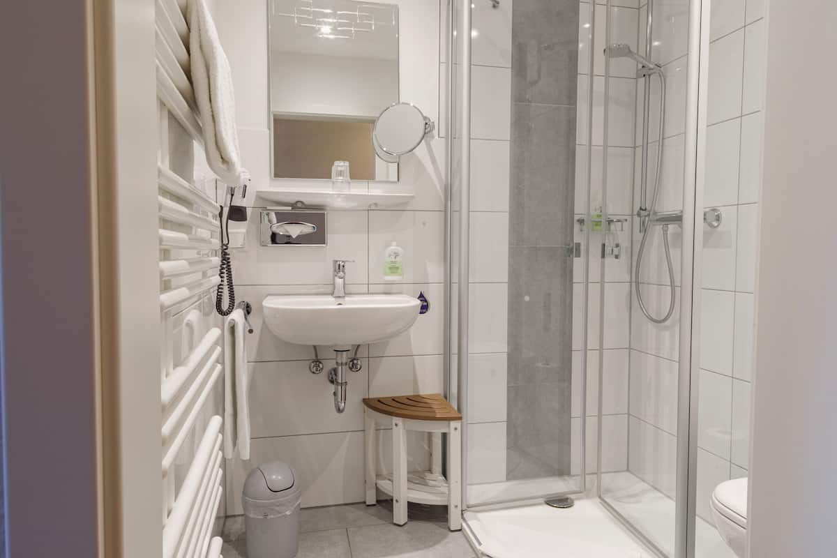 Een badkamer met een wit wastafelmeubel, een spiegel, een douche en een klein houten krukje.