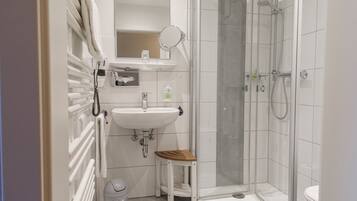 Un baño con un lavamanos blanco, un espejo, una ducha y un taburete de madera.