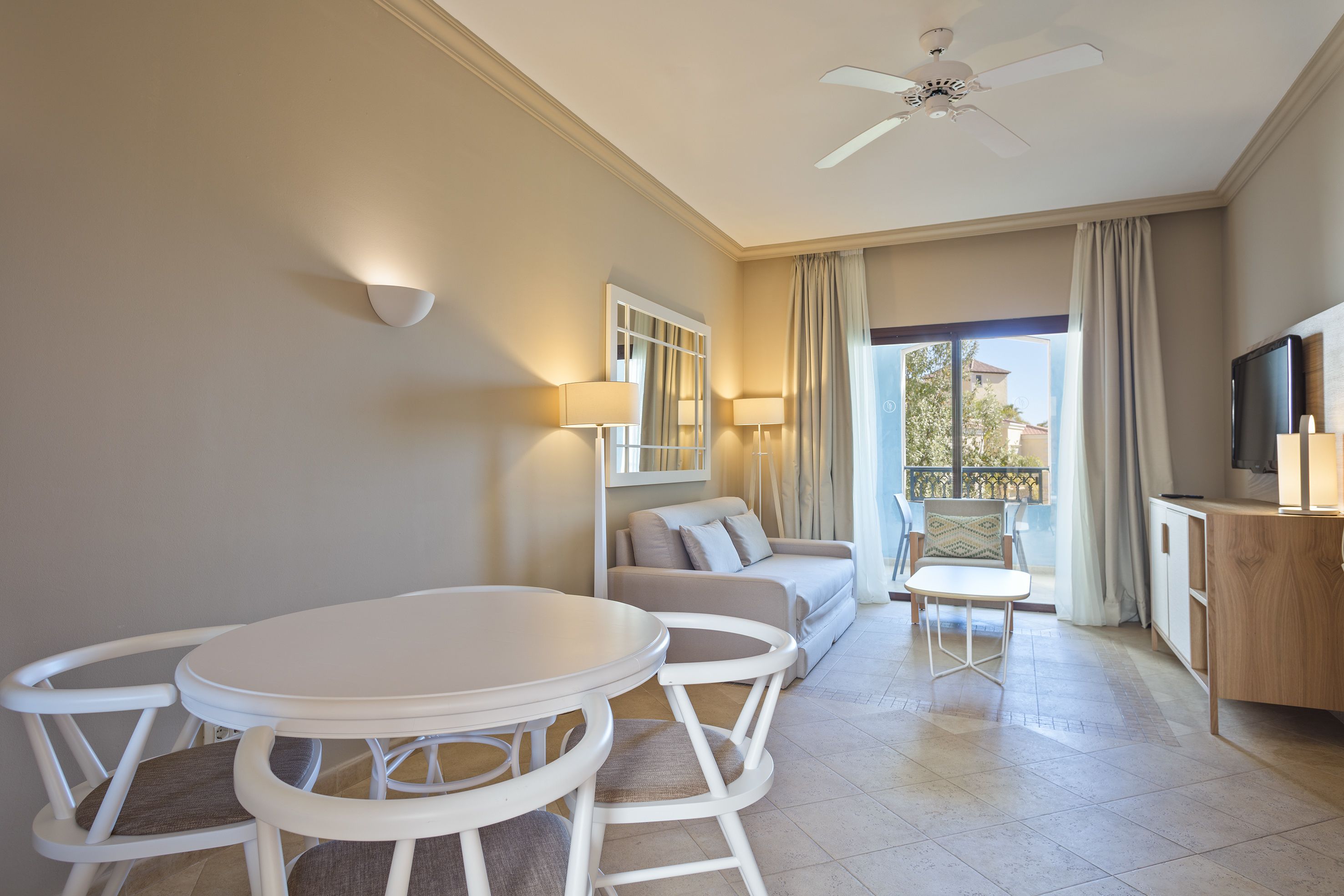 A modern living room with a round dining table, white chairs, a sofa, and a TV.
