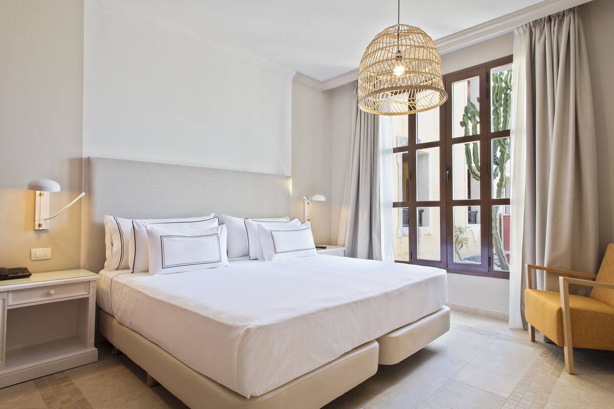 A hotel room with a large bed, bedside lamps, a chair, and a window with curtains.