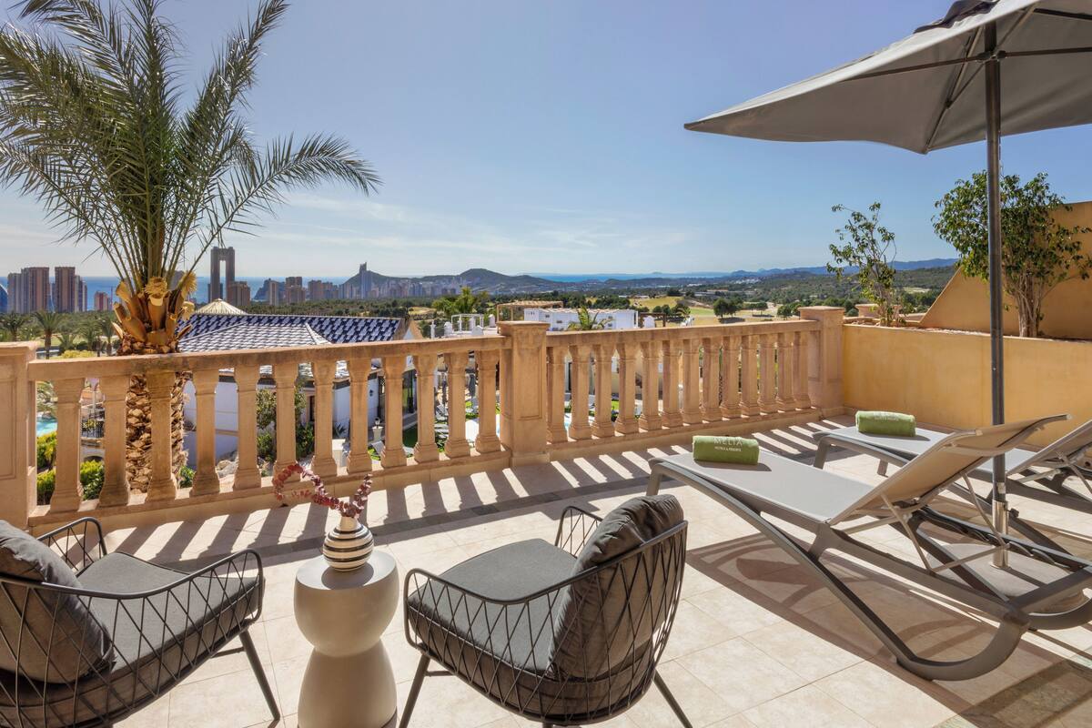 A rooftop terrace with a view of the city skyline, palm trees, and a pool.
