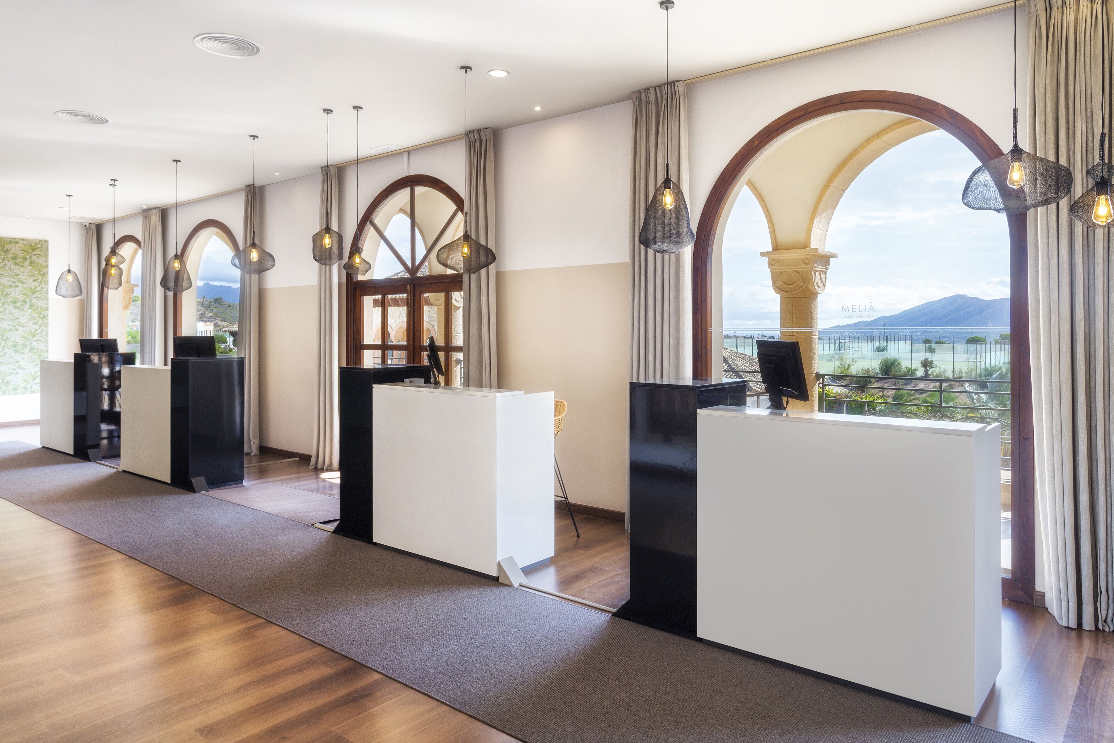 A modern hotel lobby with a reception desk, large windows, and a view of the mountains.