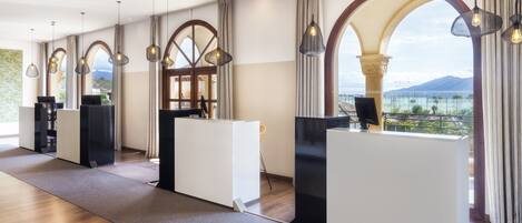 A modern hotel lobby with a reception desk, large windows, and a view of the mountains.
