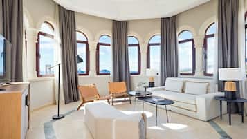 A spacious living room with a modern sofa, a coffee table, and a seating area with a chair. Large windows with curtains provide natural light and views.