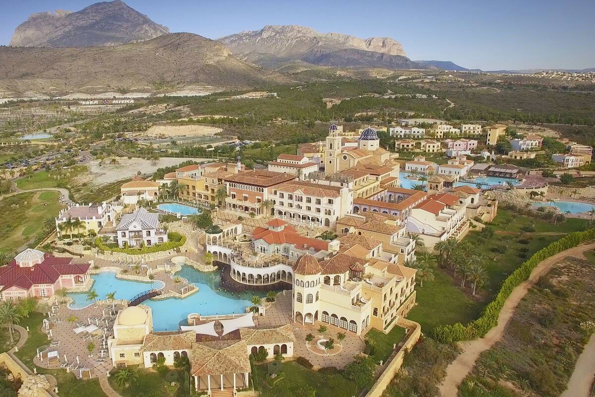 A resort with multiple swimming pools, a central courtyard, and a mountainous backdrop.