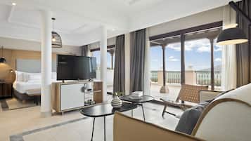 Habitación de hotel con cama, televisión, escritorio, balcón con vistas y zona de estar.