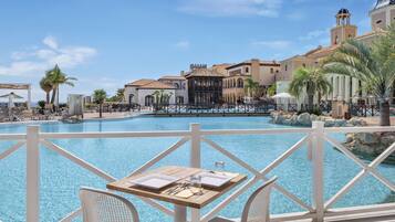 Zona de piscina con una mesa dispuesta para comer, vista despejada de la piscina y un edificio con una torre de campanas al fondo.