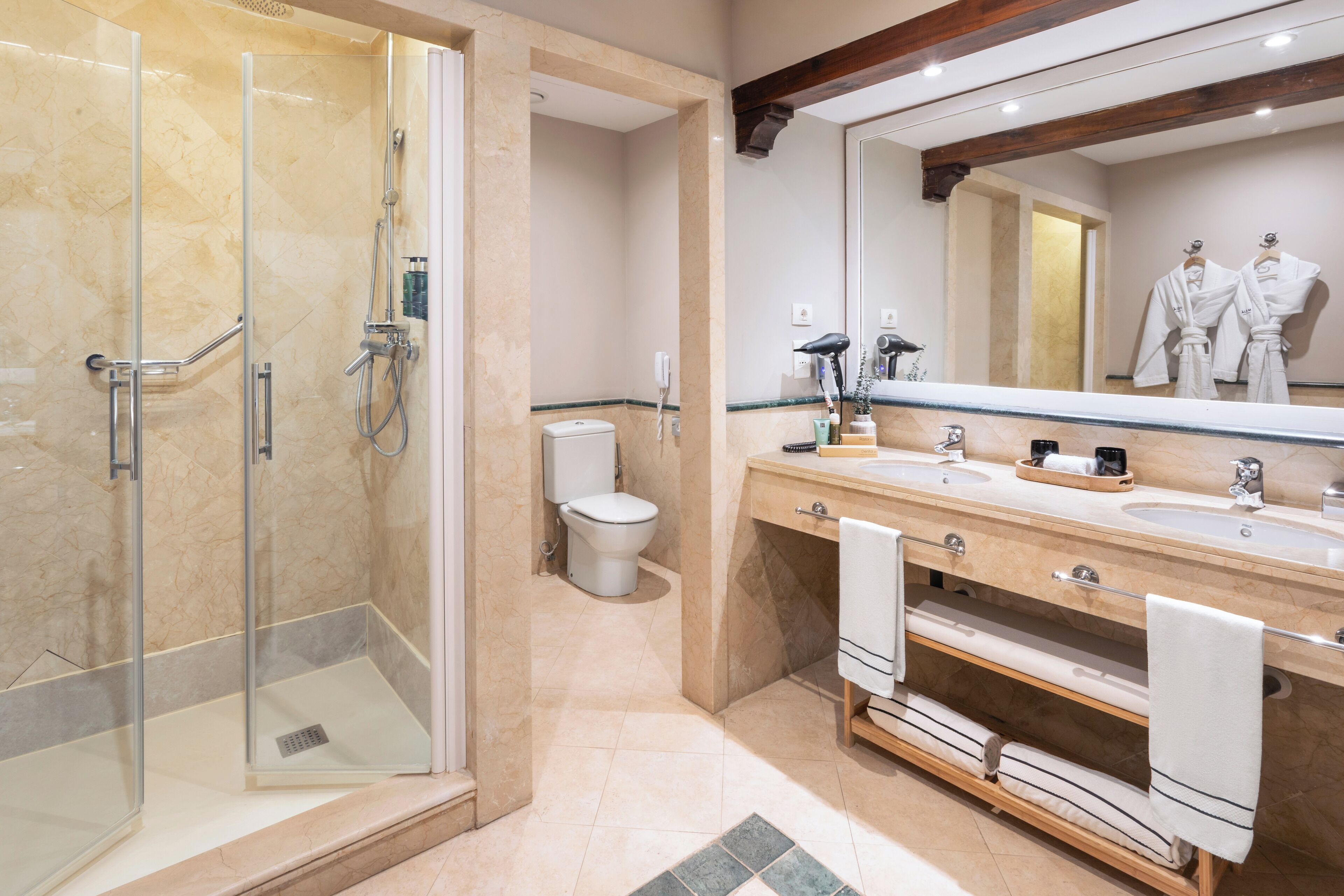 Une salle de bain moderne dotée d’une douche à parois de verre, de toilettes et d’un meuble-lavabo avec deux vasques et un grand miroir.