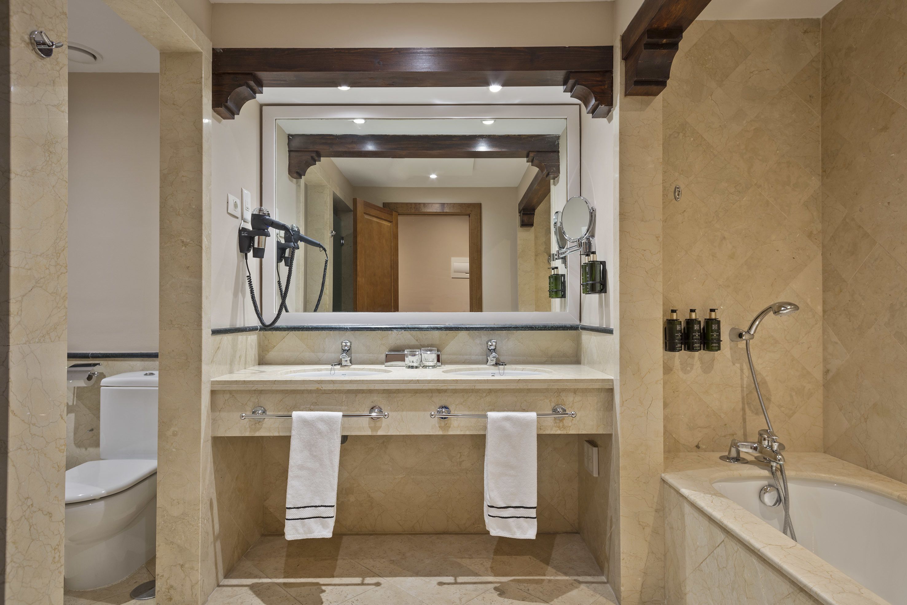 A bathroom with a large mirror, two sinks, a shower, and a toilet.