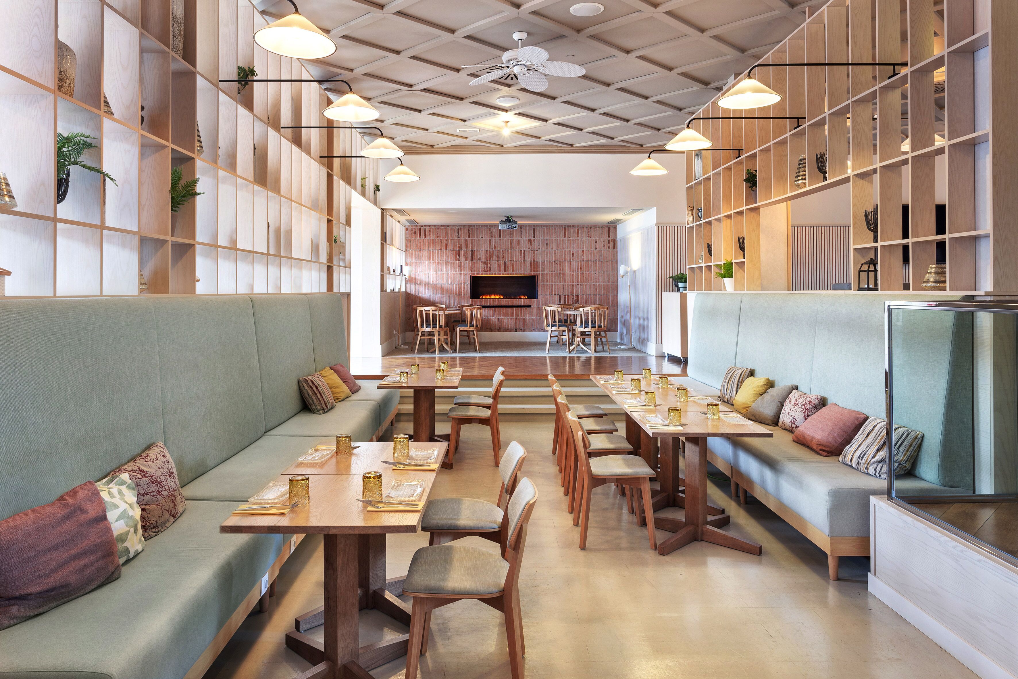 A modern restaurant with wooden furniture, a central fireplace, and pendant lighting.