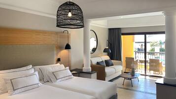 Habitación de hotel con dos camas grandes, un sofá, una mesita y un balcón con muebles de mimbre.