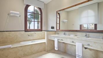 Un baño con bañera, dos lavamanos, un espejo grande y una ventana con vista a palmeras.