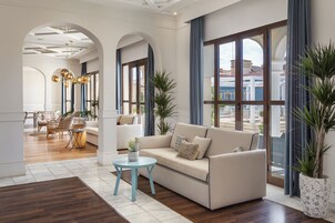 A spacious living room with a beige sofa, a small round table, and a large window with blue curtains.
