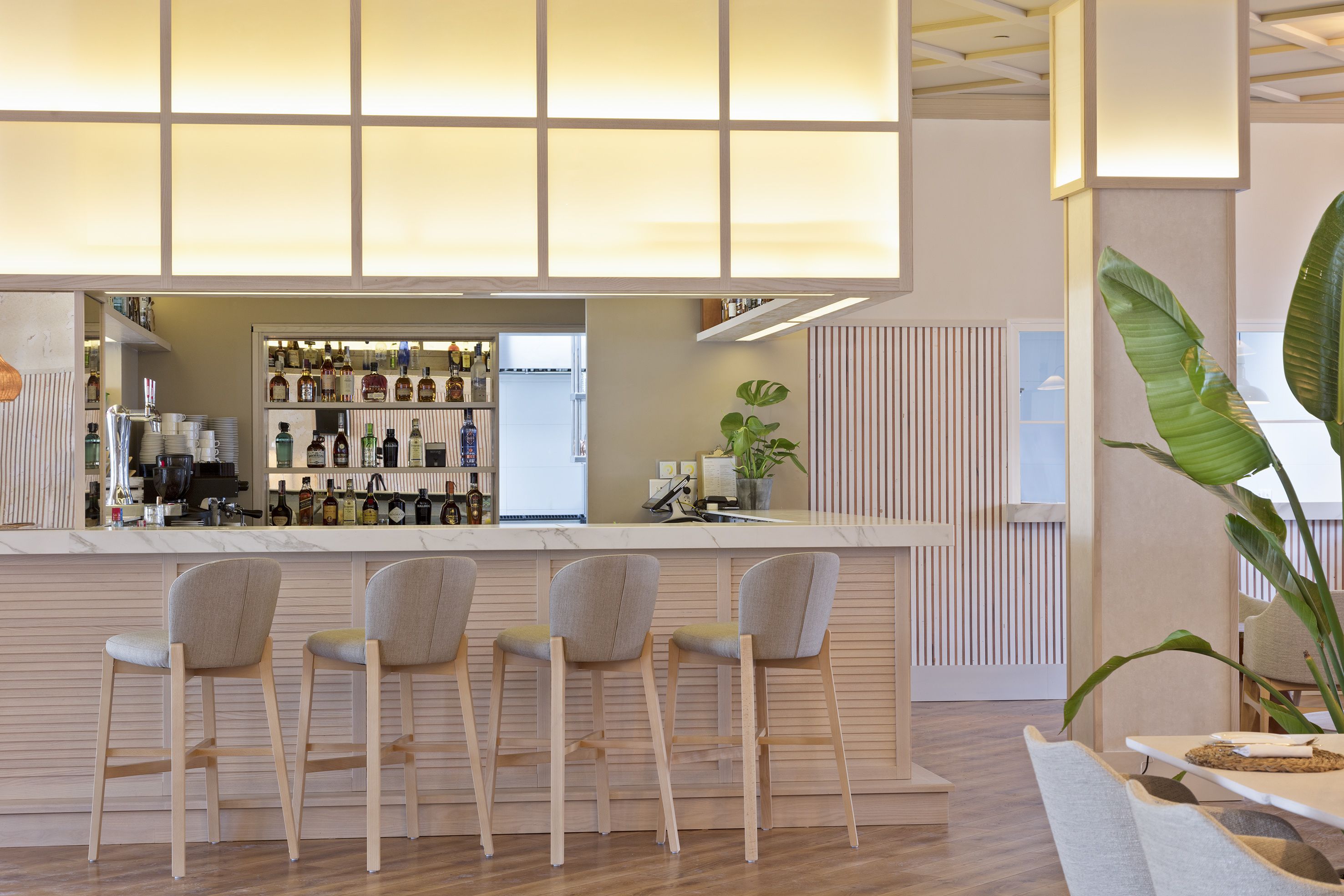 Eine moderne Bar mit einer Marmorplatte, drei Barhocker und einer Auswahl an Flaschen und Gläsern.