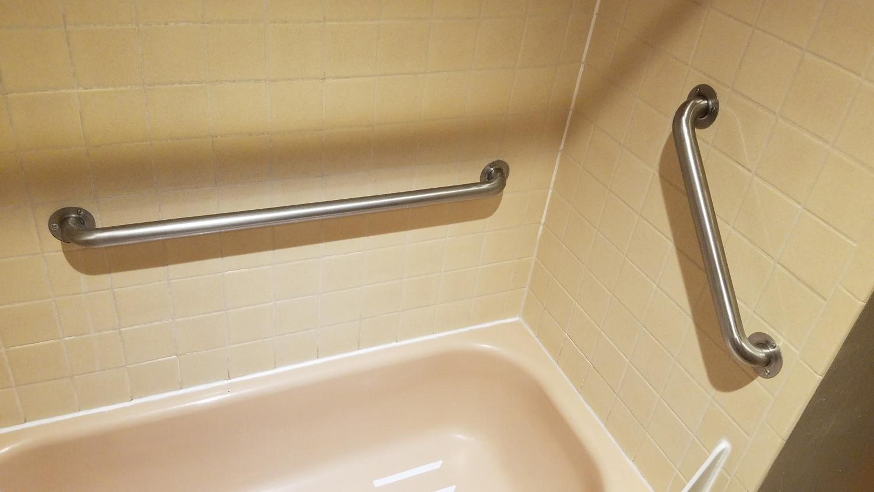 Un baño con bañera, barra de apoyo y zona de ducha.