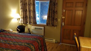A hotel room with a bed, a desk, a chair, a telephone, a window with curtains, and a door. - Royal Motor Inn (La Grande)