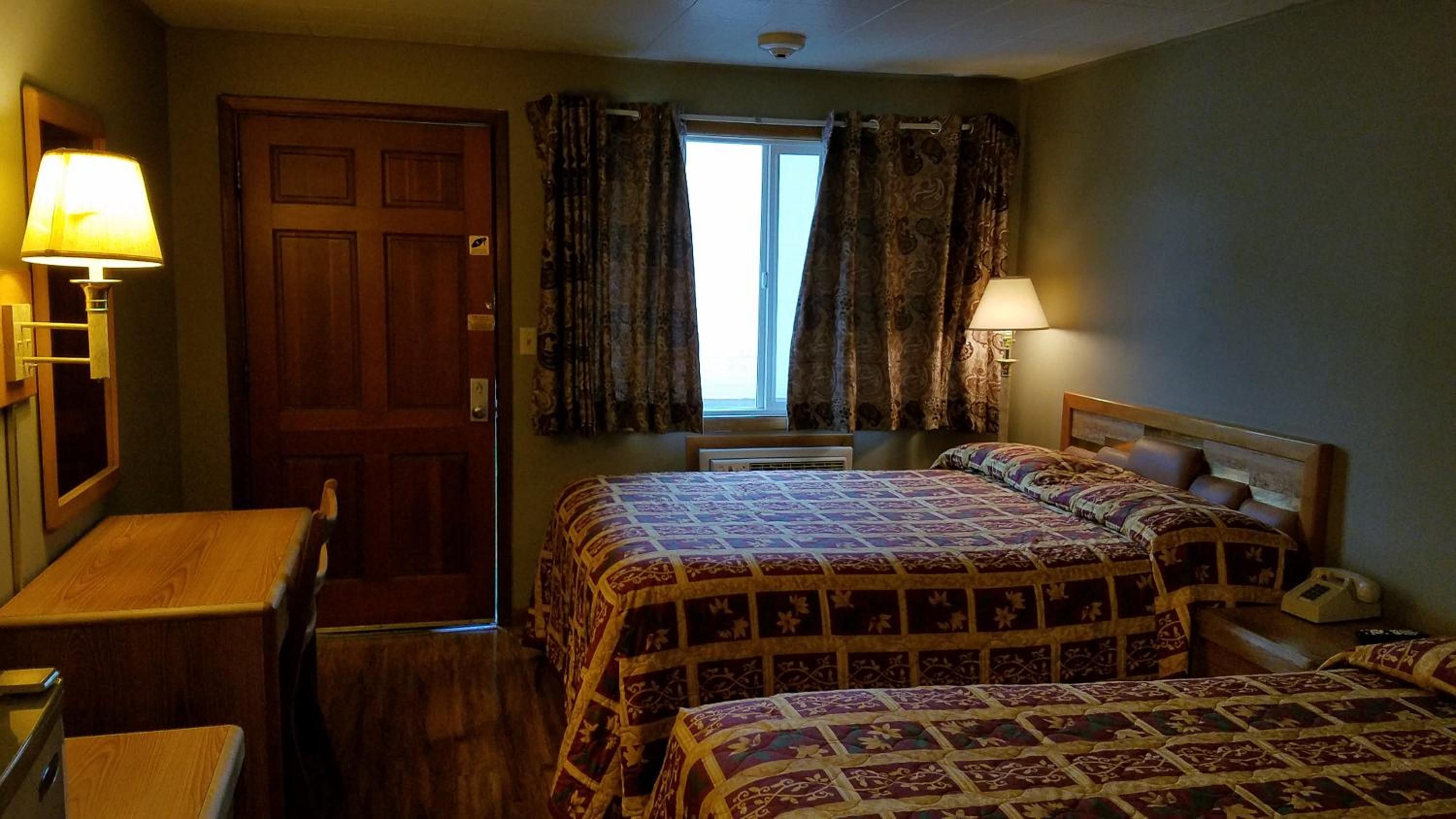 A hotel room with two beds, a desk, a chair, a window with curtains, and a door.