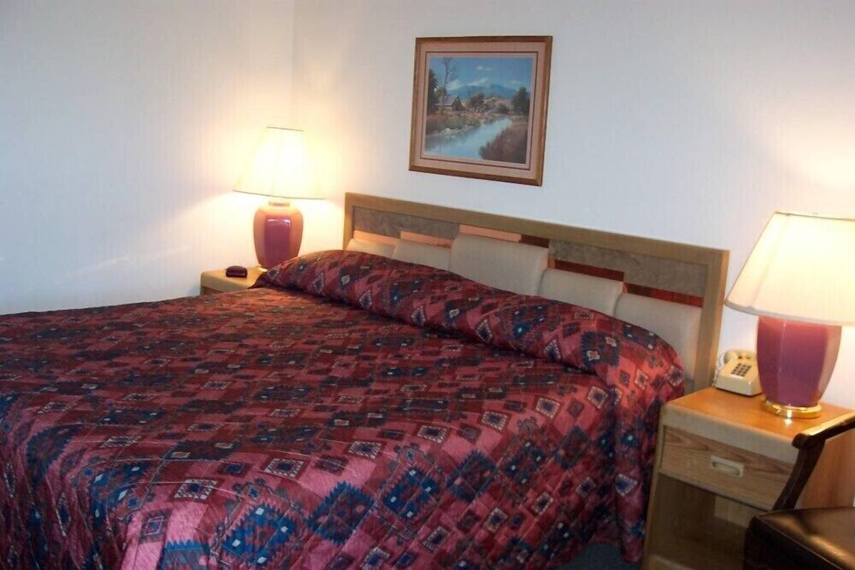 A hotel room with a bed, two bedside tables with lamps, a nightstand, and a painting on the wall.