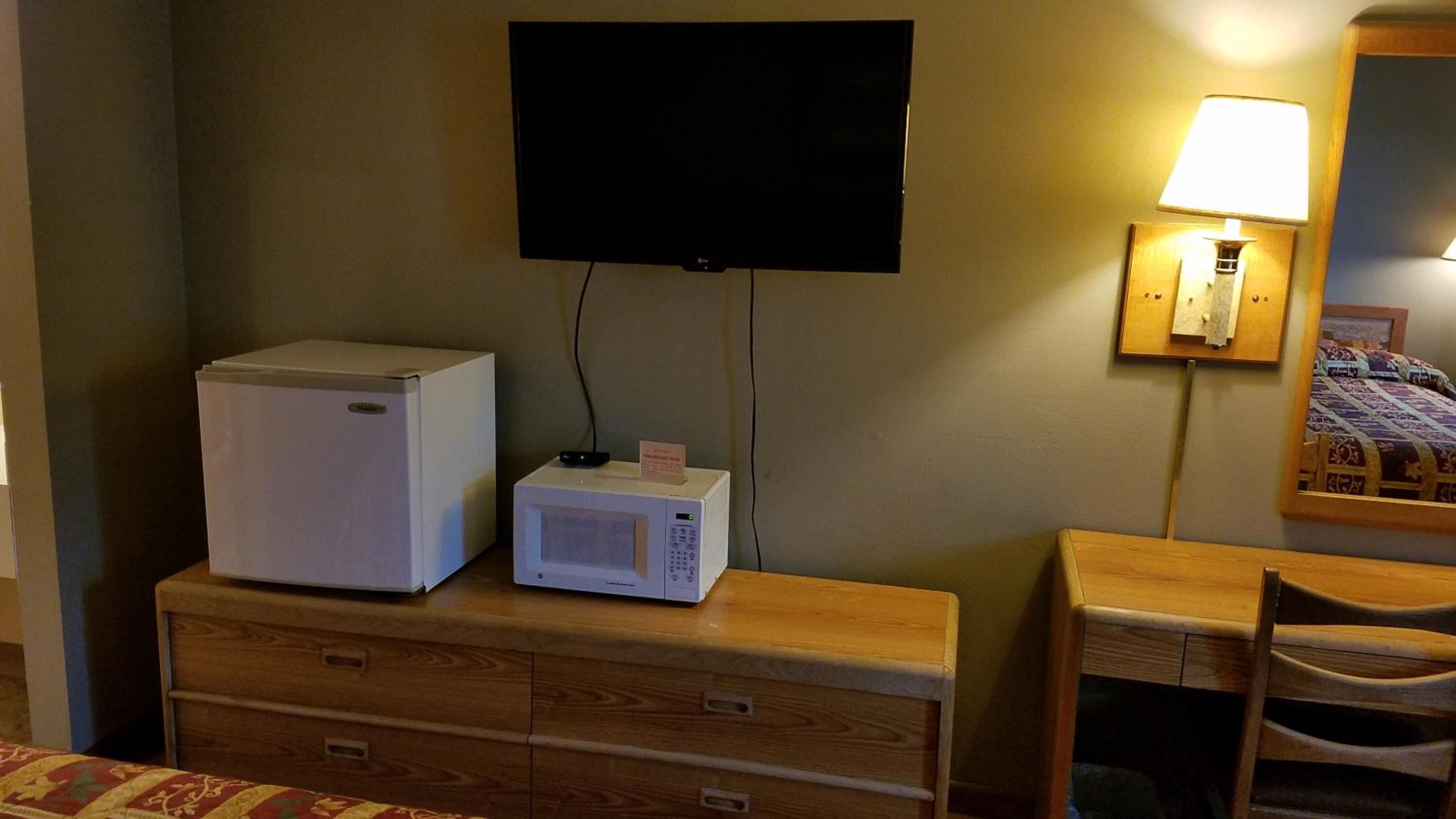 A hotel room with a wooden dresser, a microwave, a television, and a bedside lamp.
