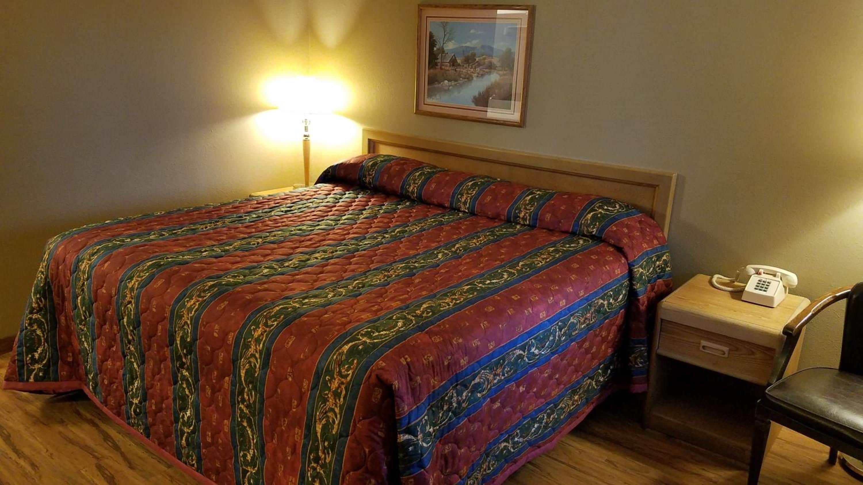 Una habitación de hotel con una cama grande, una mesita de noche con lámpara, una silla y un cuadro en la pared.