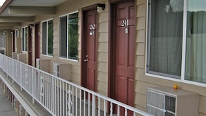 Une rangée de chambres de motel avec des portes numérotées, une rambarde blanche et des fondations en pierre.