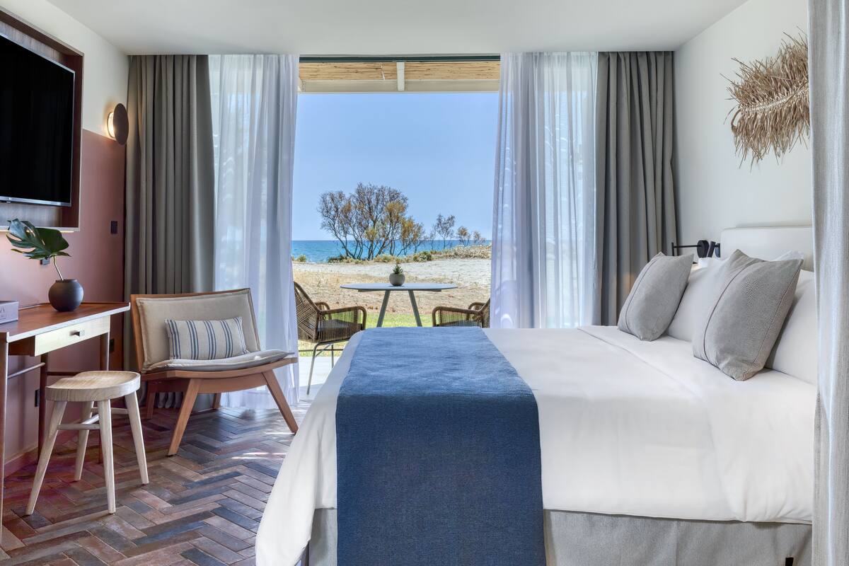 A hotel room with a bed, a desk, a chair, and a view of the beach.