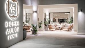 Eine moderne Hotellobby mit einer zentralen Sitzgruppe, Blumentöpfen und einem gut sichtbaren, beleuchteten Schild.