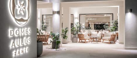 A modern hotel lobby with a central seating area, potted plants, and a prominent illuminated sign.