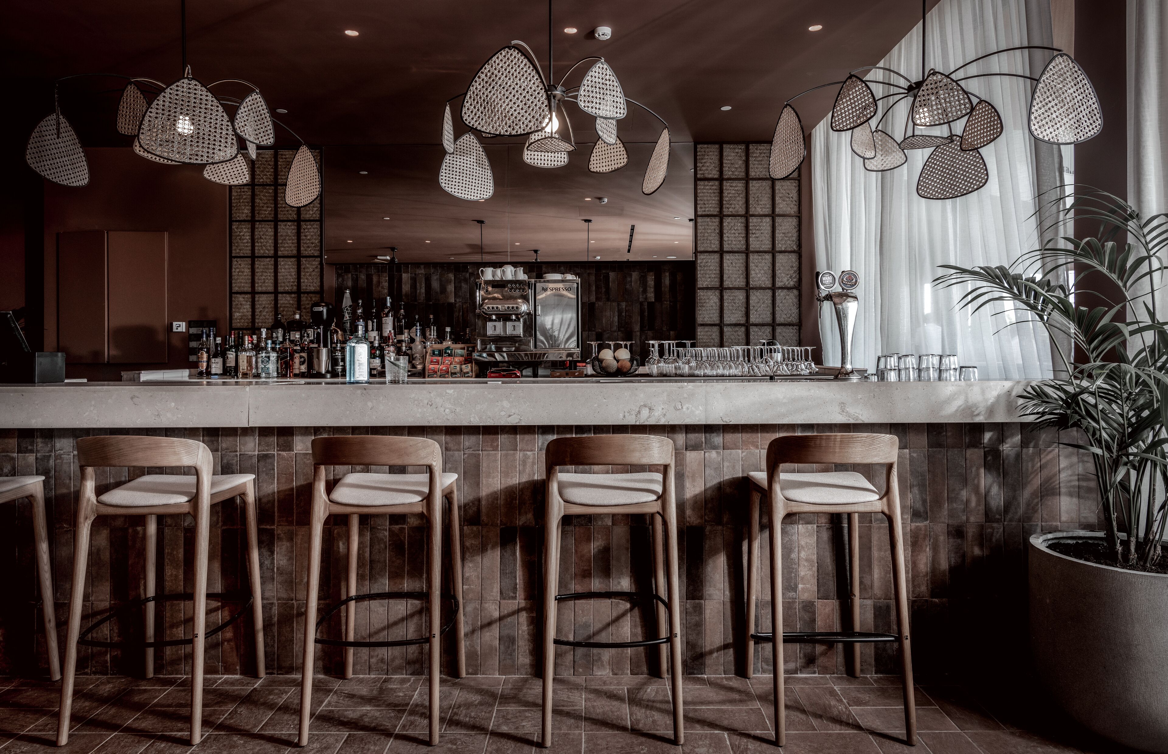 Una zona de bar con taburetes de madera, una barra y lámparas colgantes.