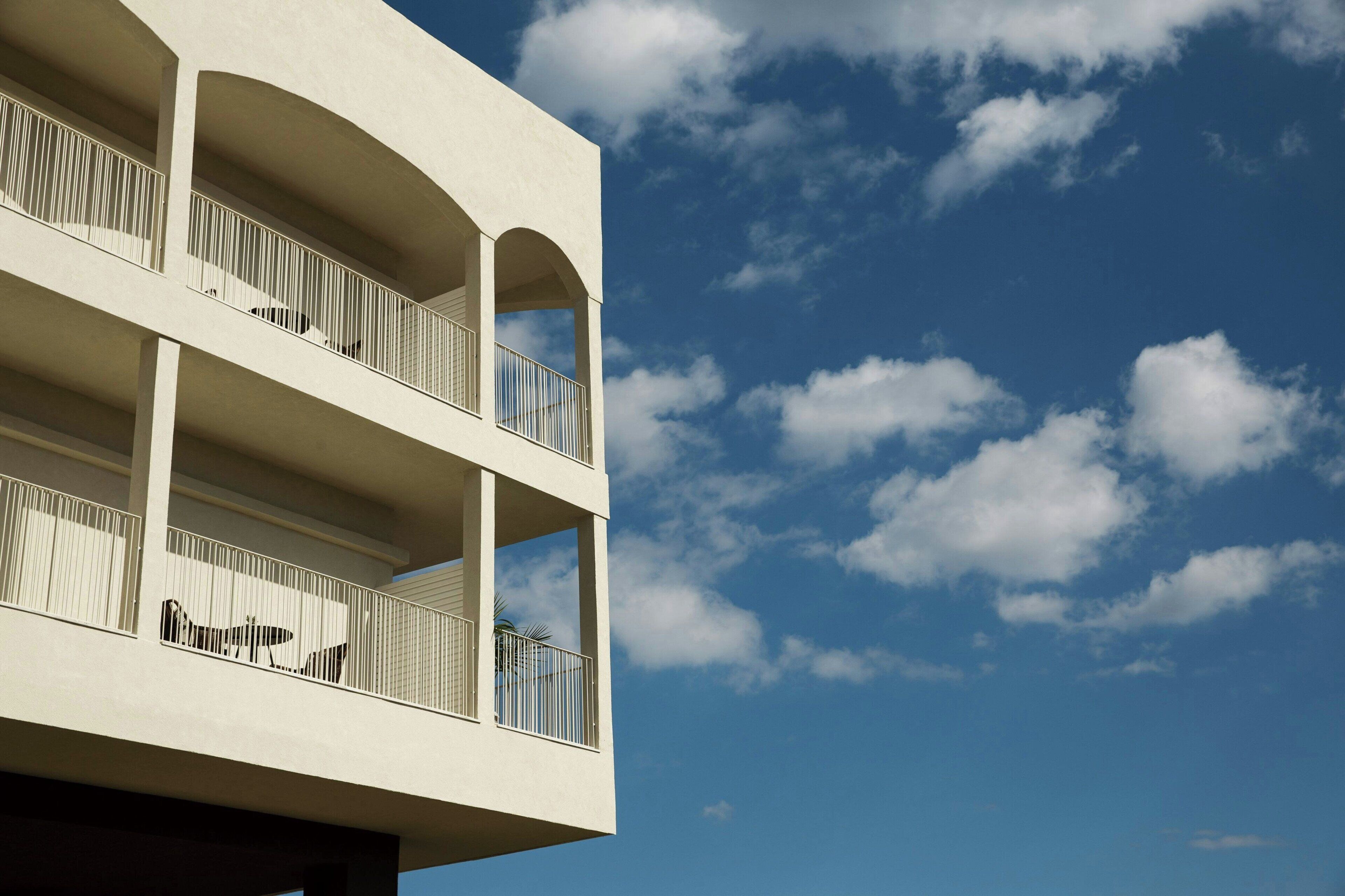 A multi-story building with balconies and a clear blue sky with clouds.