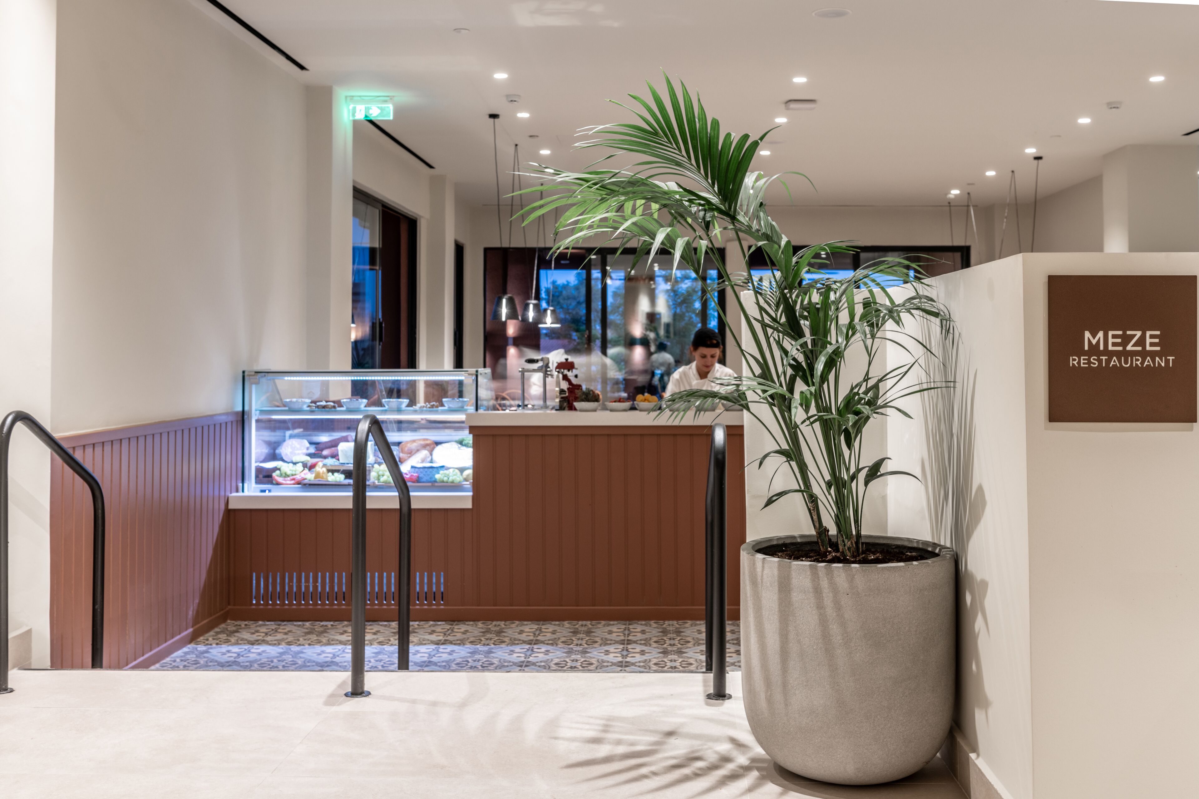 A modern restaurant interior with a wooden counter, a large potted plant, and a sign that reads "MEZE RESTAURANT."