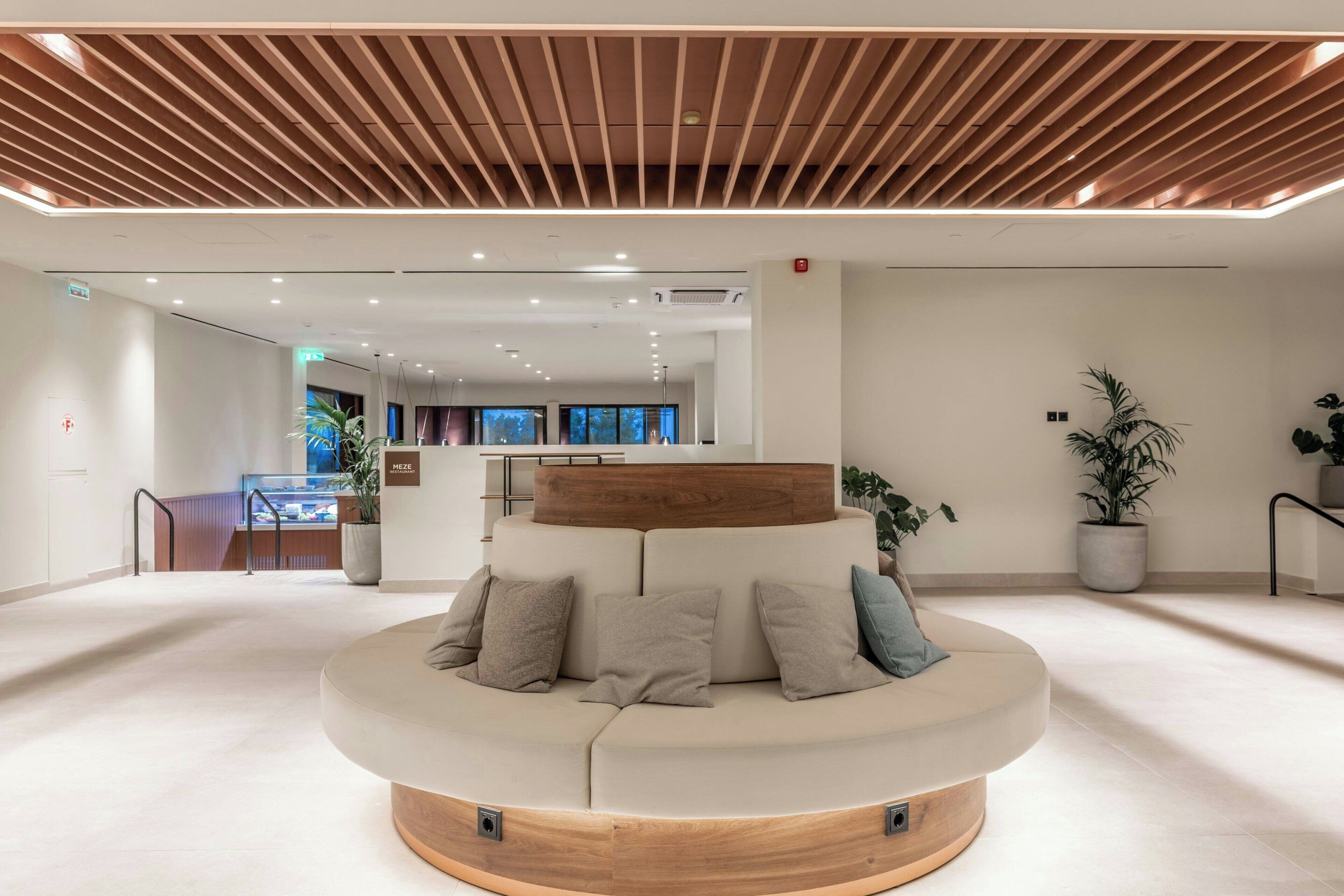A modern lobby with a circular seating area, a wooden ceiling, and potted plants.