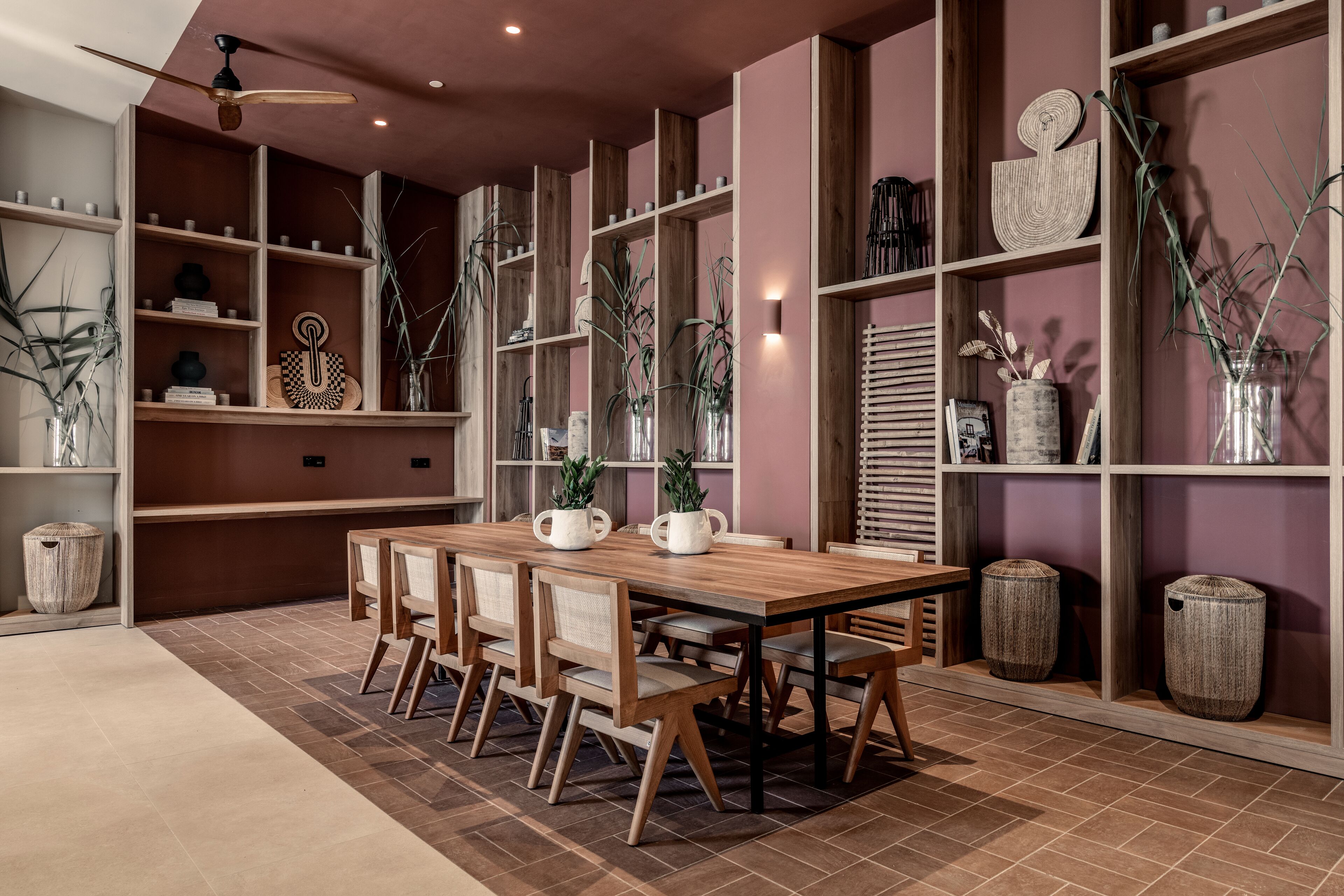 Un espace de salle à manger moderne, avec une table et des chaises en bois, entouré d’étagères ornées d’objets décoratifs et de plantes.
