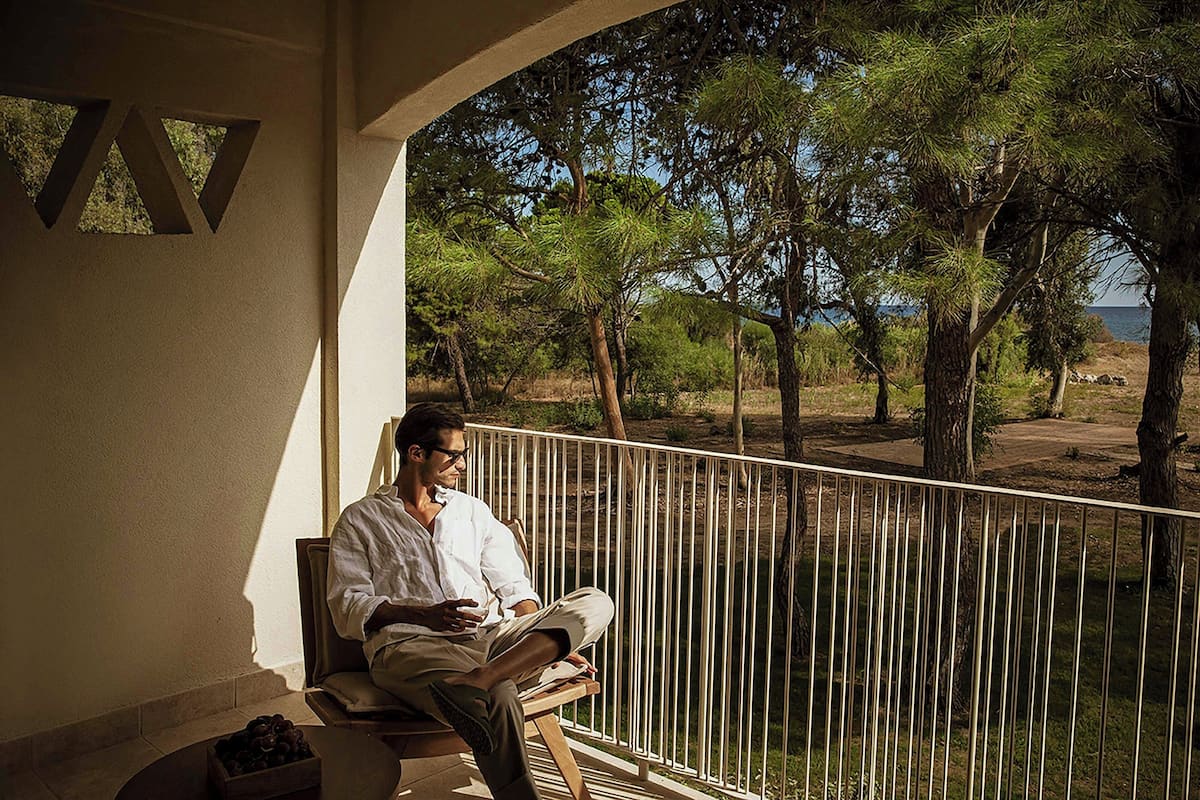A man sitting on a bench with a view of trees and a body of water.