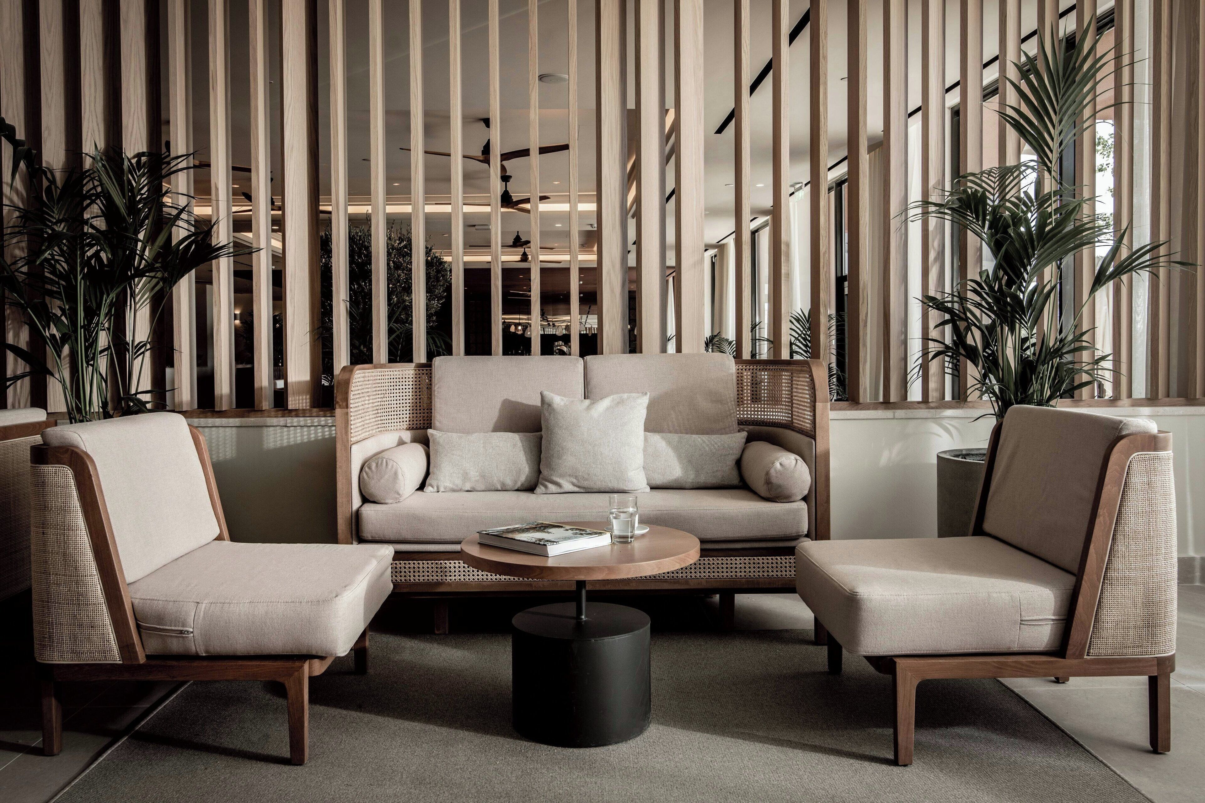 Un área de estar moderna con un sofá, dos sillones, una mesa redonda de centro y paneles de madera altos.