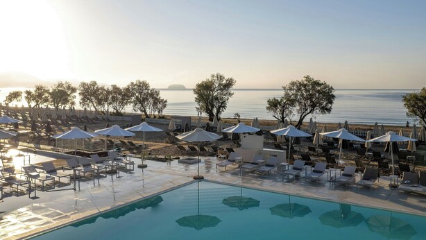 Ein Poolbereich mit Liegestühlen und Sonnenschirmen, mit Blick auf ruhiges Wasser und eine entfernte Insel.