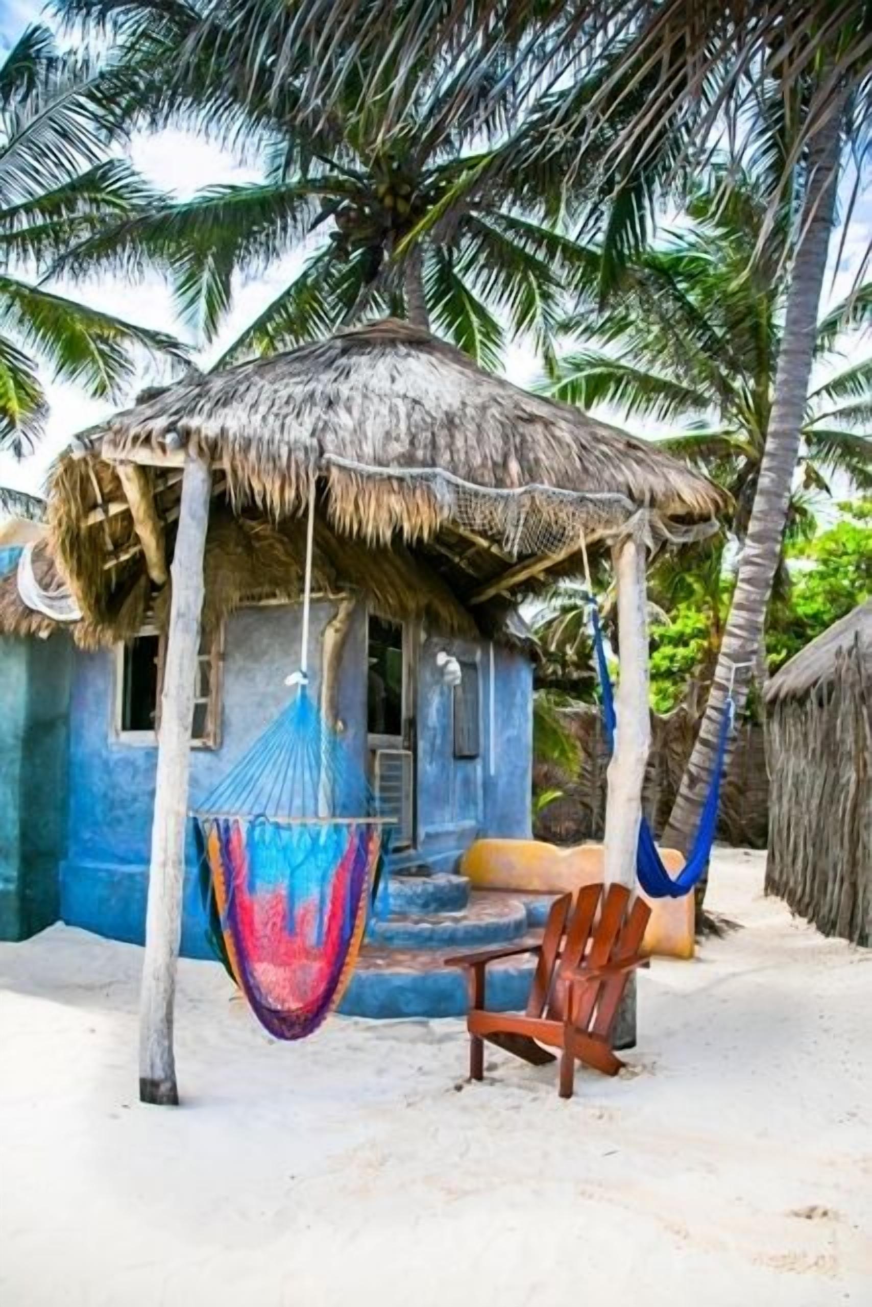 A thatched-roof hut with a hammock and a wooden chair outside.