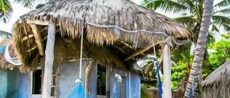 A thatched-roof hut with a hammock and a wooden chair outside.