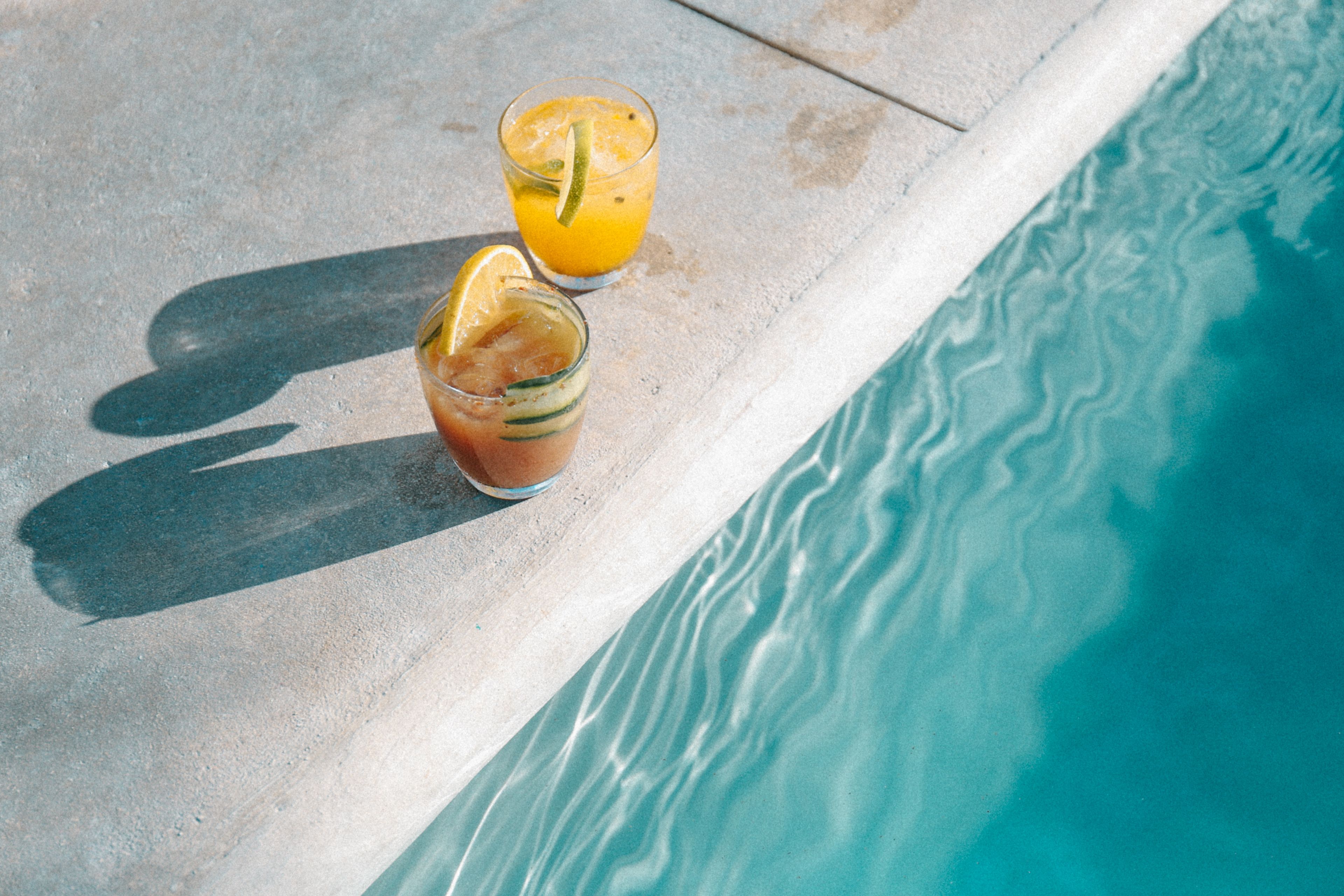 Two glasses of beverages on a poolside surface.