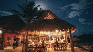 Um restaurante à beira-mar com telhados de palha e mesas ao ar livre.