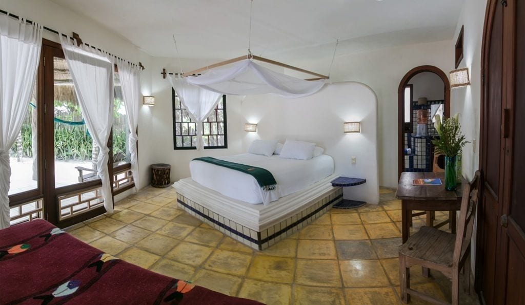 Un dormitorio con cama, mesita de noche, silla, mesa y ventana con cortinas.