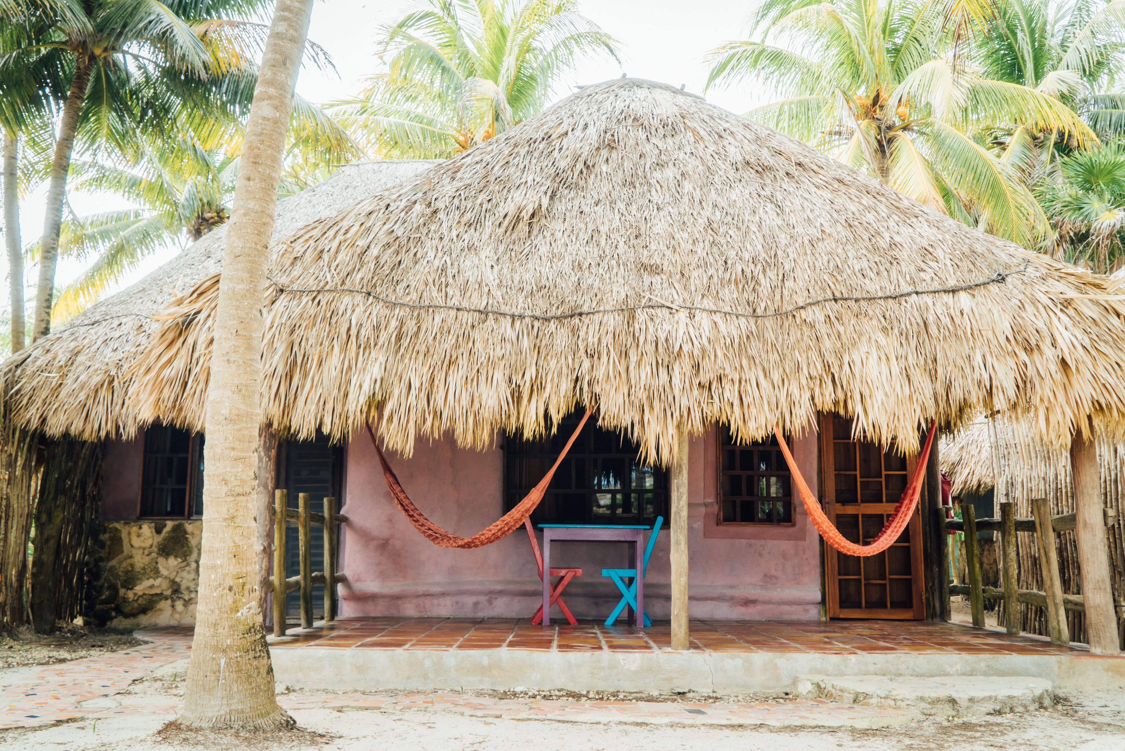A thatched-roof hut with a hammock and a table outside.