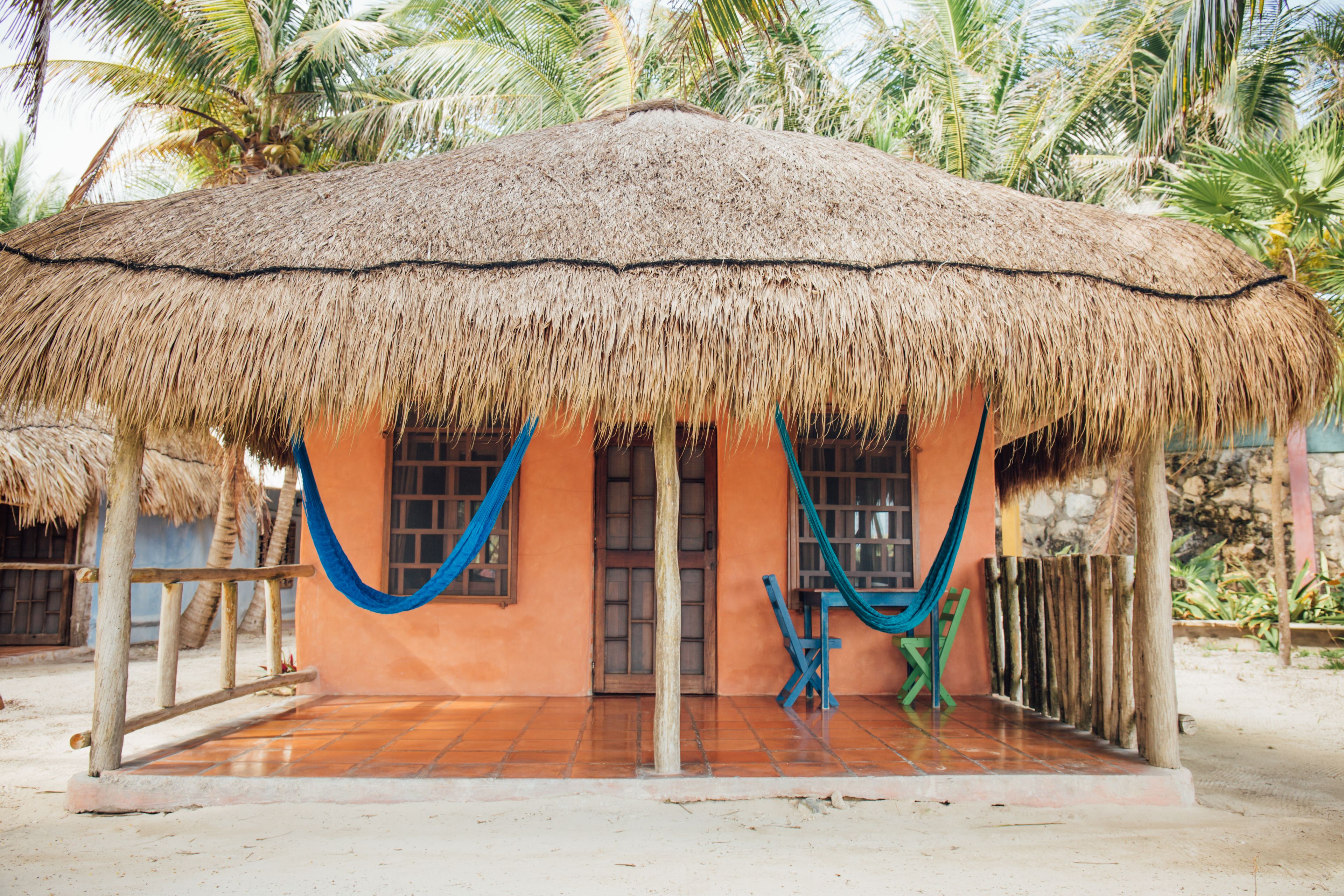 A thatched-roof hut with a tiled floor, a wooden door, and a window.
